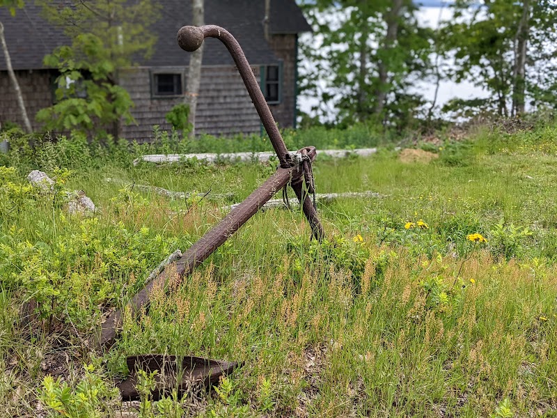 Rusted anchor lies in tall grass near a rustic building in Brooksville, Acadia National Park.