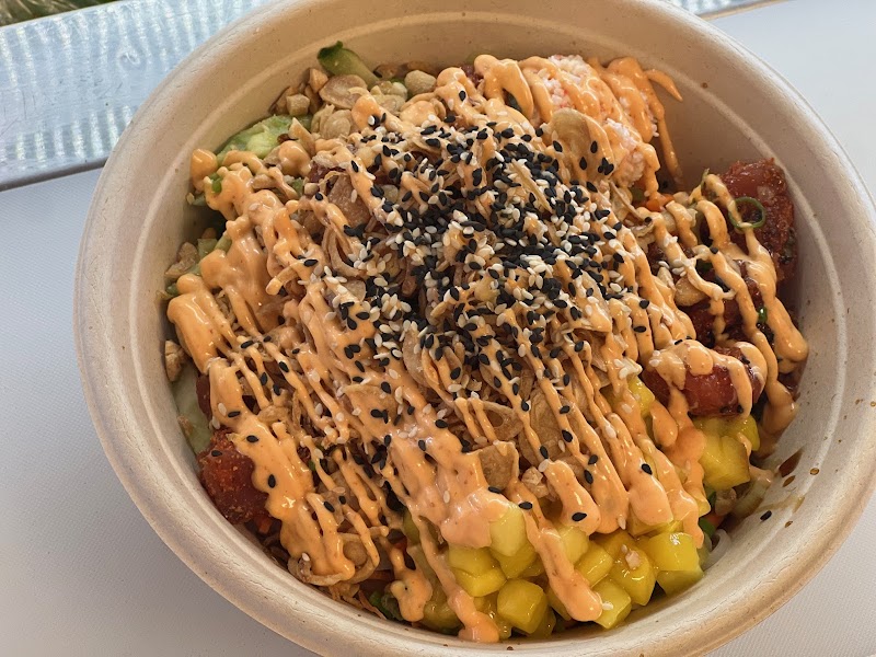 Bowl of yellow mango and green avocado chunks with browned protein, orange drizzle, and black sesame seeds, Acadia National Park.