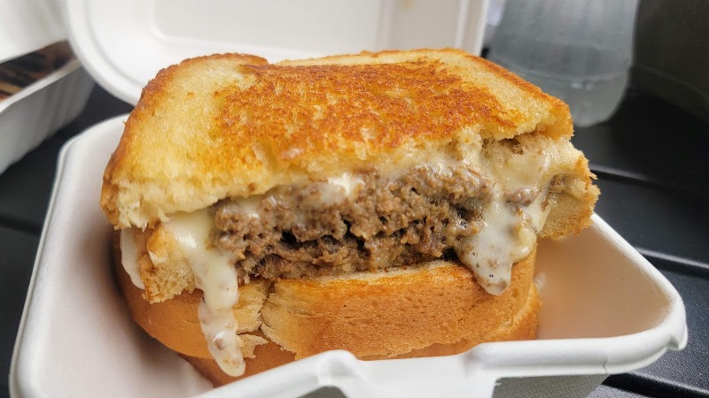 Toasted burger with melted cheese and beef patty in a white takeout container at Acadia National Park.