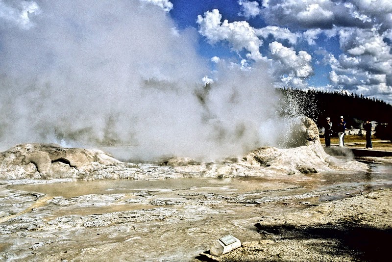 Steam vents bubble from mineral terraces at Sunset Lake, Yellowstone National Park, with visitors in the background.