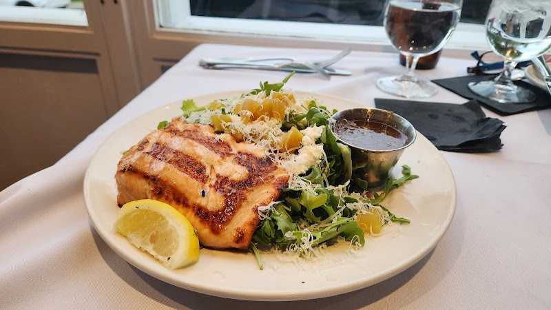 Grilled salmon with lemon wedge atop greens salad, shredded cheese, and a side sauce on a plate at Acadia National Park.