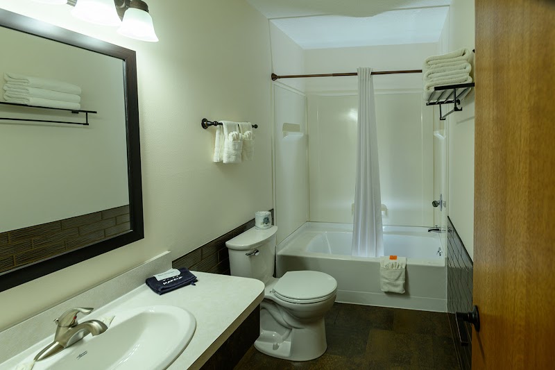 Bright en suite bathroom with sink, mirror, toilet, tub with shower curtain, stacked towels, and dark tile floor in Badlands National Park.
