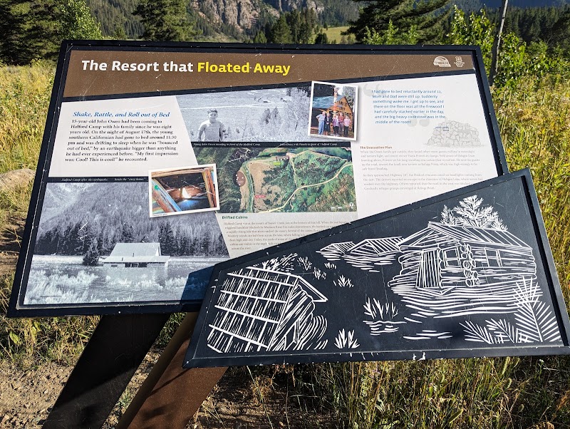 Informational signboards at Refuge Point Trailhead, Yellowstone National Park, featuring maps, historical photos, and a drawing of a log cabin.
