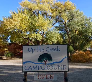 Arches National Park campground sign reading Up the Creek Campground, surrounded by autumn trees and blue sky.