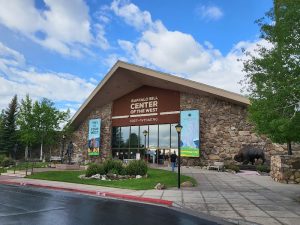 Stone visitor center exterior near Cody, Wyoming, with banners in Yellowstone area under a blue sky.