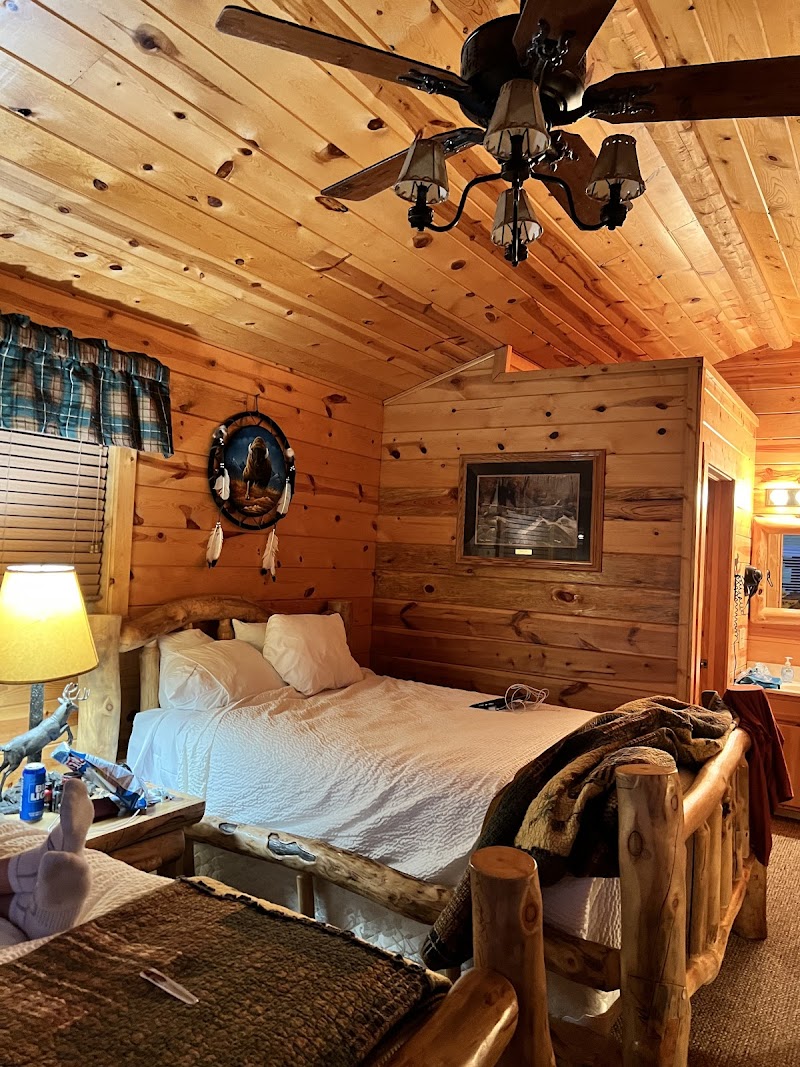 Cozy rustic bedroom in a log cabin with a white bed, wooden walls, ceiling fan, dreamcatcher wall decor, and framed art at Badlands National Park.