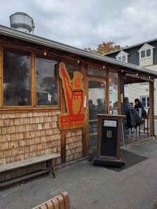 Wooden clapboard restaurant exterior with a red parrilla sign, string lights, and outdoor seating in Acadia National Park.