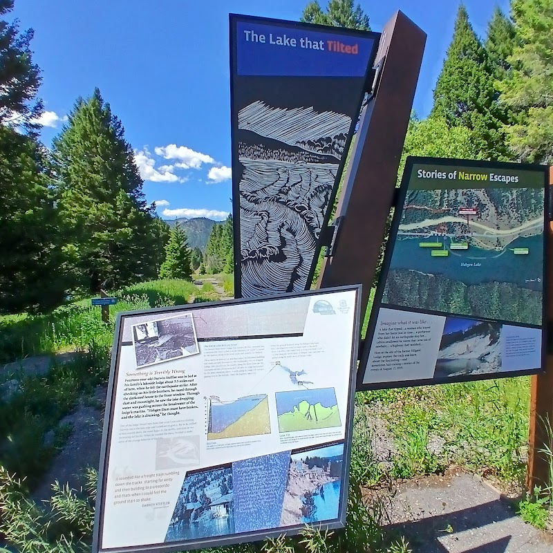 Earthquake Lake informational panels with diagrams and maps overlooking pines and meadows in Yellowstone National Park.