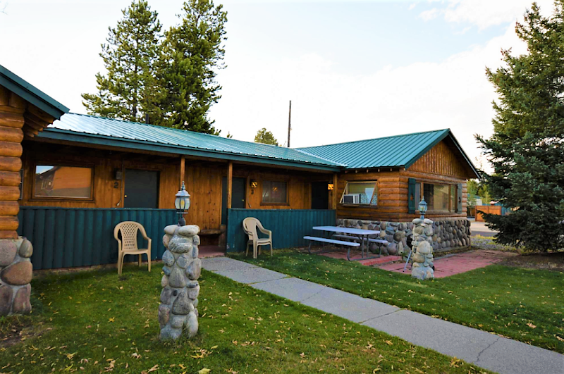 Single-story log lodge with teal metal roof, stone pillars, chairs, and a picnic table in Yellowstone National Park.