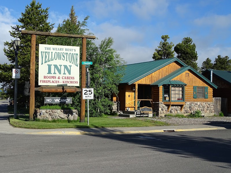 A rustic wooden lodge with a stone base and green roof beside a large lodging sign, in Yellowstone National Park.