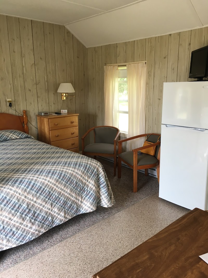 Cozy Acadia National Park lodging room with plaid bedspread, wooden dresser, lamp, two chairs, window, and a white refrigerator.