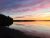 Sunset over a calm inlet with pink-orange sky, forested shoreline left, and mirror-like water at Acadia National Park.