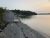 Pebbled shoreline with a small wooden cottage perched near the water's edge along Acadia National Park coastline at sunset.