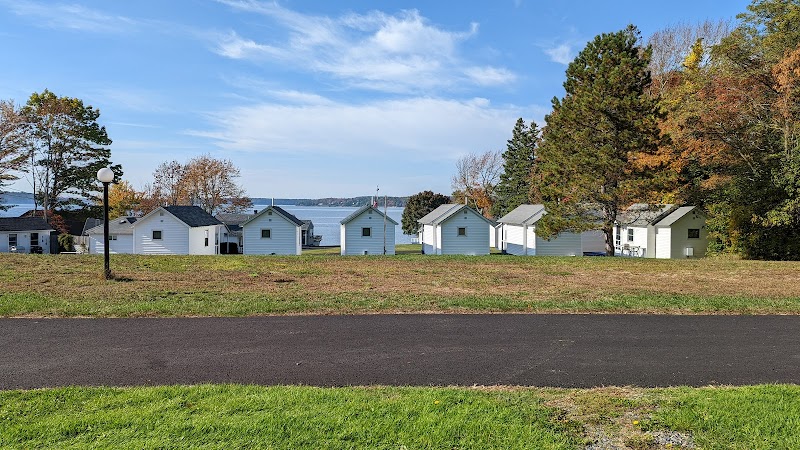 Row of white cottages along a grassy shore with a paved path, trees, and a lake in Acadia National Park.