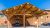 Wooden lodge entrance with a large log porte-cochère, benches, and a parked car outside under a blue sky in Yellowstone National Park.
