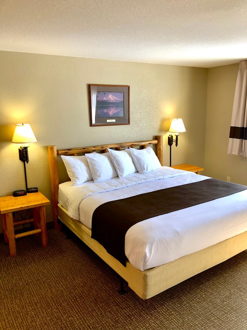 Cozy Yellowstone National Park hotel room with a wooden bed frame, white bedding, brown runner, two bedside tables, and warm lamps.