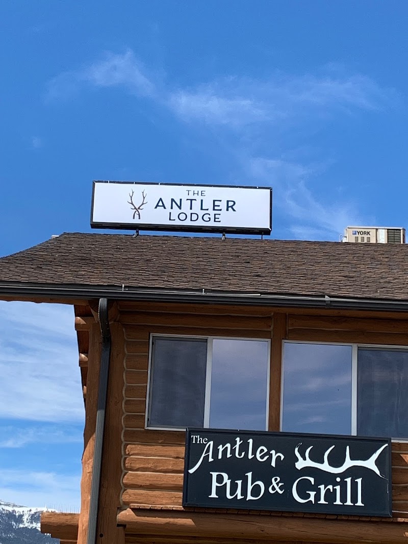 Wooden lodge with a rectangular rooftop sign and a dark sign featuring antlers, under a clear blue sky in Yellowstone National Park.