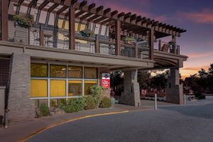 Lodging building with stone pillars, large windows glowing yellow, and a wooden second-floor terrace at Arches National Park.