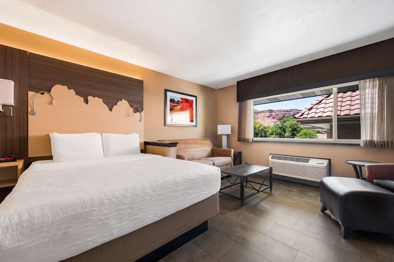 Spacious hotel room with a king bed, sofa, coffee table, and a large window showing red rock near Arches National Park.