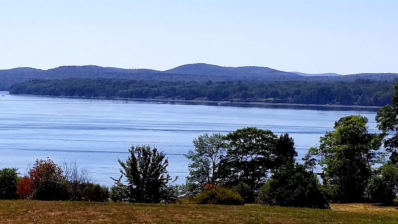 Prospect overlook in Acadia National Park features calm blue water, rolling hills, and pine trees along the shoreline.