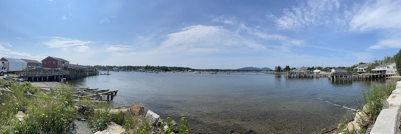 Bass Harbor harborfront in Acadia National Park, wooden piers, rocky shoreline, calm water, and a bright blue sky.