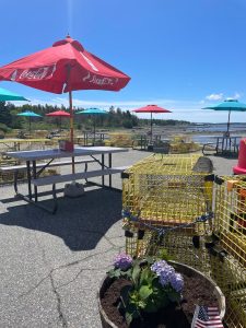 Seaside picnic area with a red Coca-Cola umbrella, turquoise parasols, lobster crates, and hydrangeas at Acadia National Park.