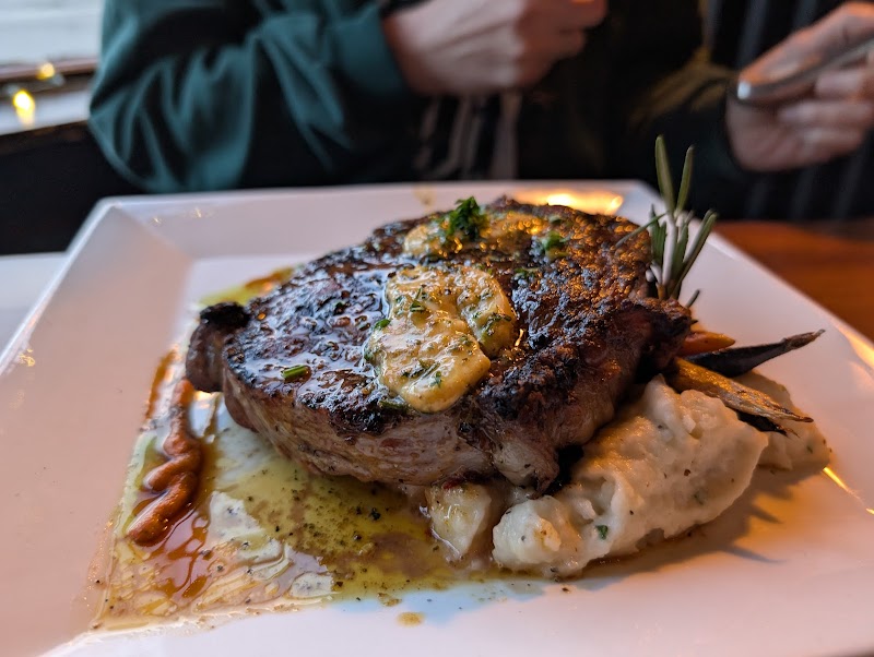 Juicy seared steak with herb butter sits on creamy mashed potatoes, with rosemary garnish, on a white plate at Acadia National Park.