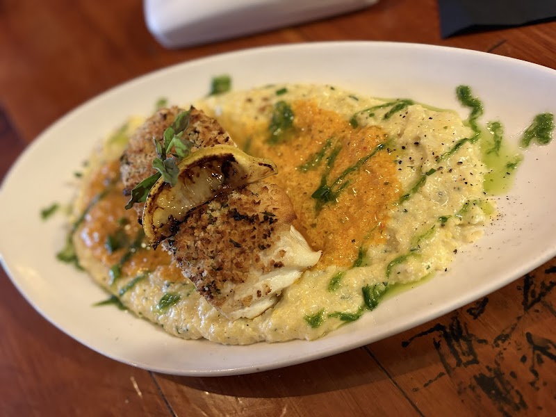 Creamy risotto with green herb oil and orange crumb, topped by a lemon-garnished fried fillet, in Acadia National Park.