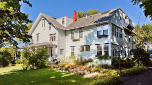 Two-story pale blue inn with a gabled roof, many windows, and a manicured garden in Acadia National Park.