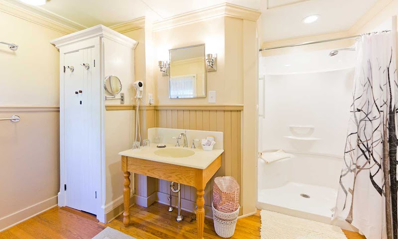 Cozy hotel bathroom with wood pedestal sink, white sink vanity, wall mirror, built-in cabinet, hair dryer, and a shower with a patterned curtain in Acadia National Park.