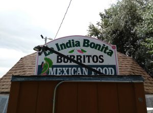 Brown wooden shack with a curved sign advertising burritos and Mexican food, set against a cloudy sky in Badlands National Park.