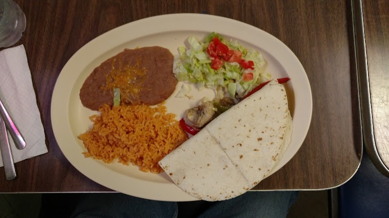 Plate at Badlands National Park shows a burrito with half tortillas, alongside rice, beans, and a small salad on a wooden table.