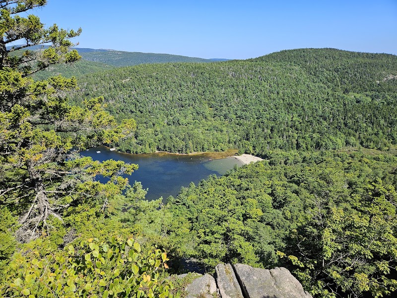 Echo Lake Beach in Acadia National Park, a blue lake edged by dense pines with a rocky overlook under a clear sky.