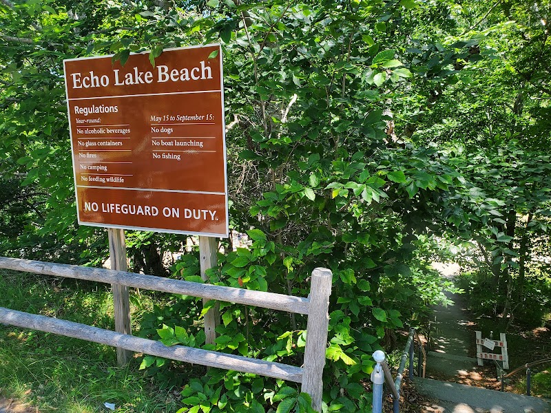 Echo Lake Beach sign with regulations, wooden railing, and dense green foliage beside a path at Acadia National Park.