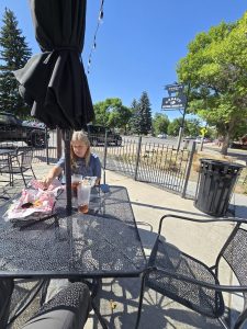 Outdoor dining on a sunny Yellowstone National Park patio with metal tables and a large umbrella.