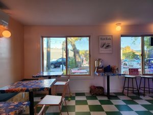 Cozy cafe interior in Acadia National Park with floral tables, white chairs, green checker floor, and string lights.