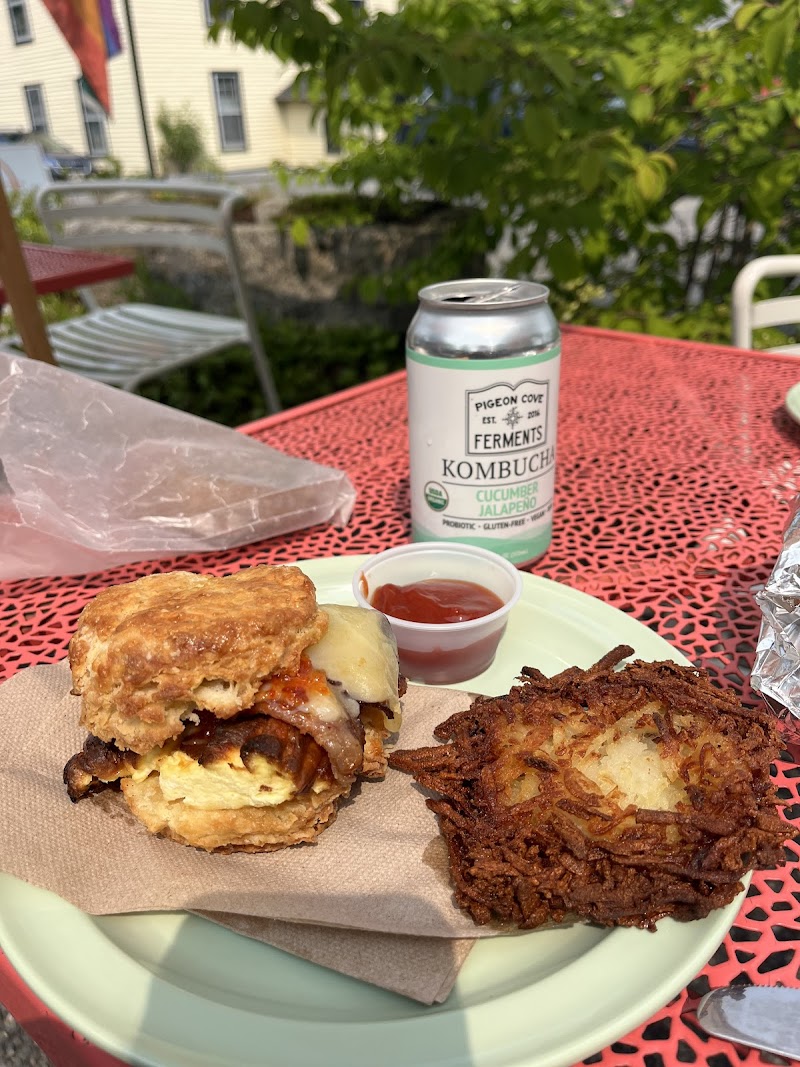 Cheeseburger with bacon and a hash brown fritter on a red metal table, ketchup cup, cucumber jalapeño kombucha, outdoors in Acadia National Park.