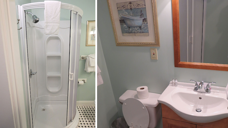 Bright bathroom with a curved glass shower, toilet and wooden vanity sink, framed art on mint-green walls in Acadia National Park.