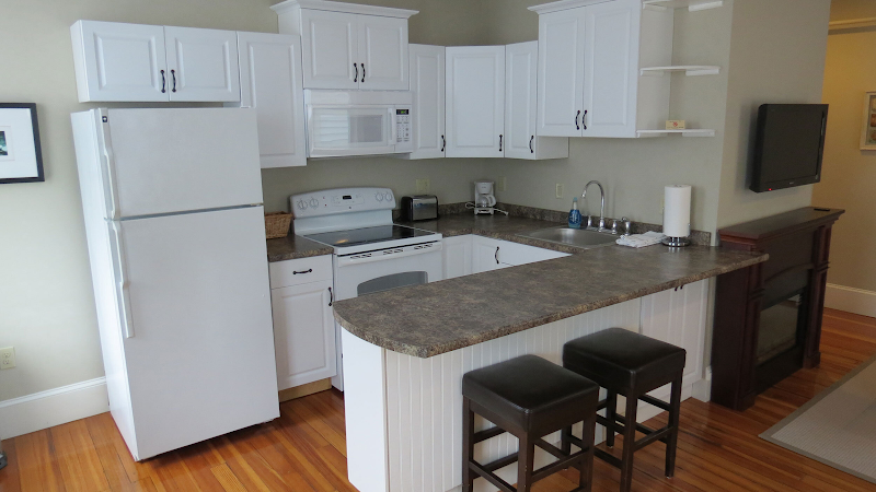 Bright white-cabinet kitchen with fridge, stove, microwave, island and two brown stools, plus a wall TV, in Acadia National Park.