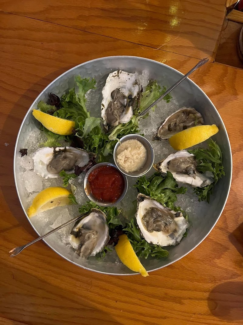 Oyster platter on ice with lemon wedges, mixed greens, and three dipping sauces, set in Acadia National Park.