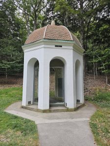White octagonal pavilion with a tiled dome sits among trees at the Sieur de Monts site in Acadia National Park.