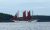 Red-sailed schooner glides across calm waters along the Acadia National Park coast.