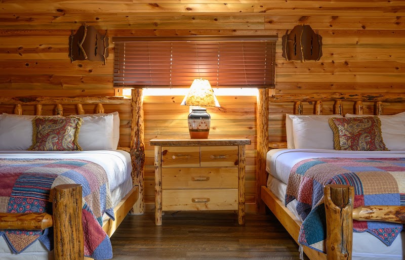 Rustic lodge bedroom with two log-frame twin beds, quilts, and a wooden nightstand with a lamp in Badlands National Park.