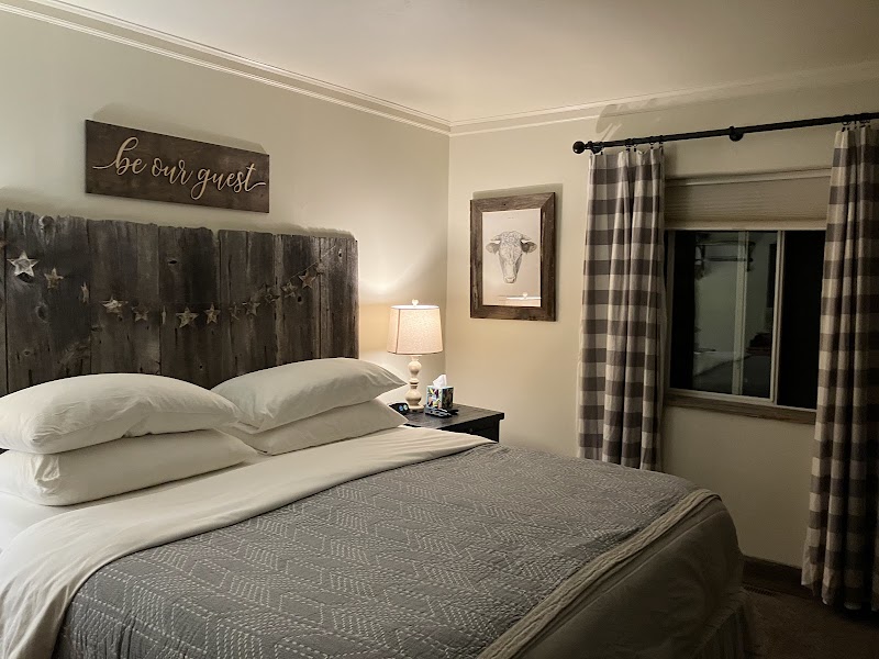 Cozy rustic bedroom with a weathered wooden headboard, star garland, lamp, cow artwork, and checkered curtains in Badlands National Park.
