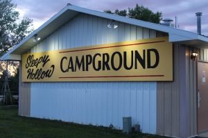 Exterior view of a wooded campground entrance with RV sites and a rustic sign