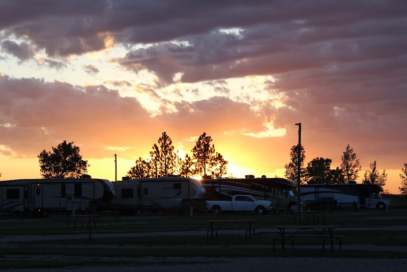 Sunset over a row of RVs and trailers at a campground with silhouetted trees in Badlands National Park.