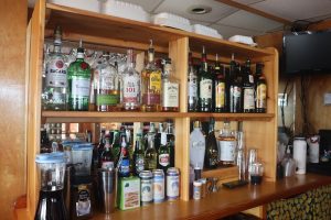 Interior bar area inside a restaurant located in Acadia National Park, showing shelves full of liquor bottles and glassware.