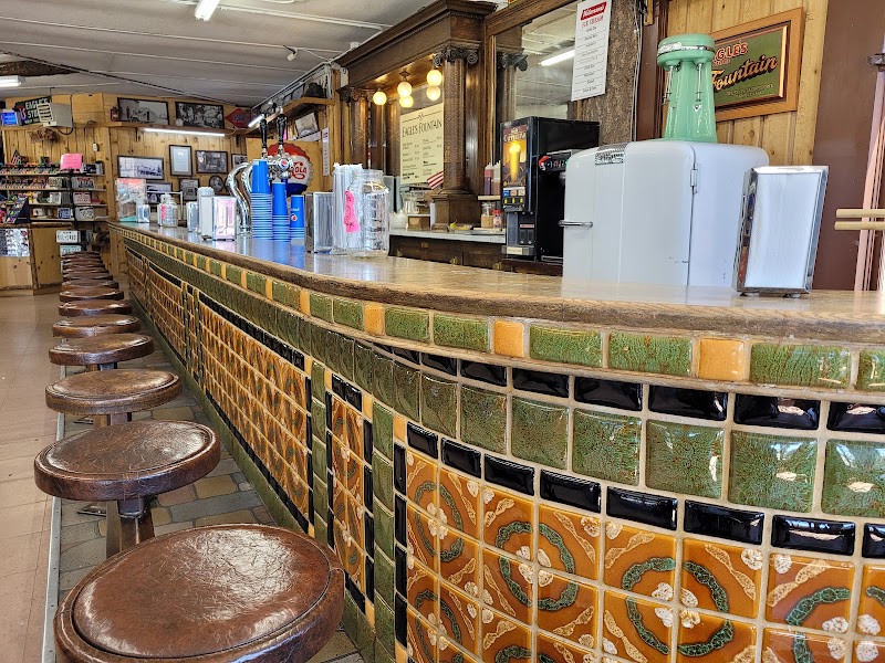 Interior of a Yellowstone National Park gift shop with a long tiled counter, green-brown mosaic walls, and wooden stools.