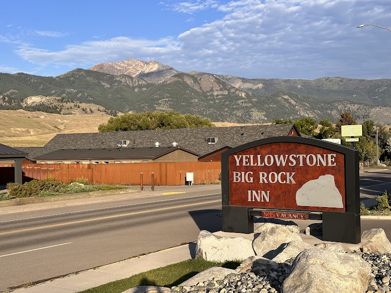 Motel along a paved road with a large red sign, rocky landscaping, and a mountain range in Yellowstone National Park.