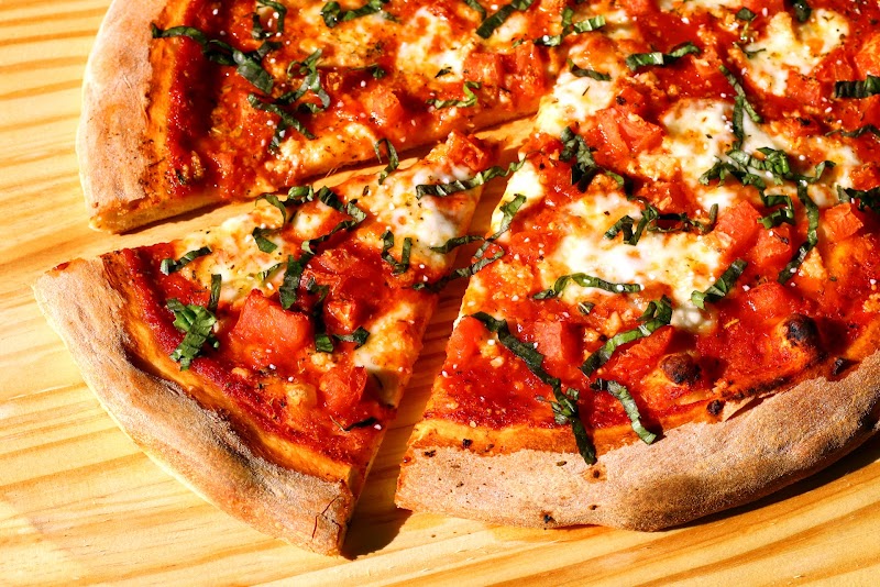 Wooden board with a cheese and tomato pizza slice, scattered torn basil, and a crispy crust in Acadia National Park.